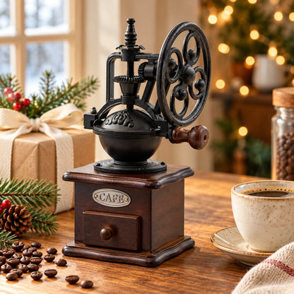 Vintage-Handkaffeemühle neben einem verpackten Geschenk, Tannenzweigen und einer Kaffeetasse im warmen Weihnachtslicht.